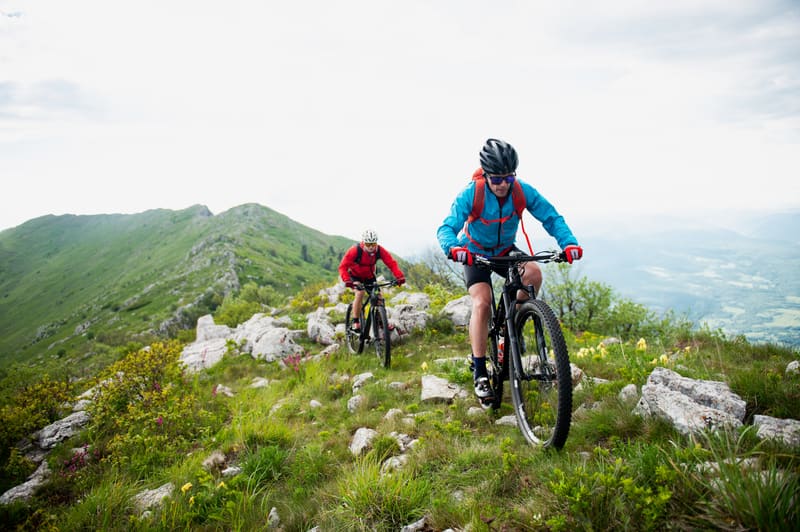 Two mountain bikers riding a grassy ridge high above a valley