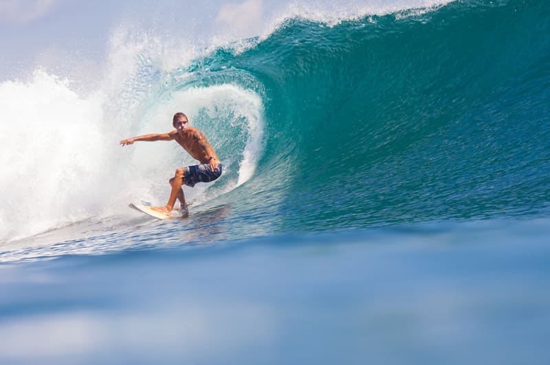 A surfer riding inside a curling turquoise wave